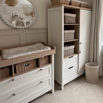Nursery room with white changing table and storage unit, featuring baskets and a mirror.