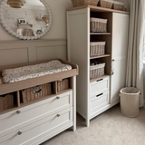 Nursery room with white changing table and storage unit, featuring baskets and a mirror.