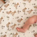 A close-up of a baby's bare foot resting on a textured cream-colored sheet printed with teddy bears and small floral motifs.