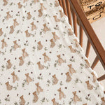 A close-up of a baby muslin blanket with a teddy bear print, draped over the corner of a wooden crib.