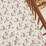 A close-up of a baby muslin blanket with a teddy bear print, draped over the corner of a wooden crib.