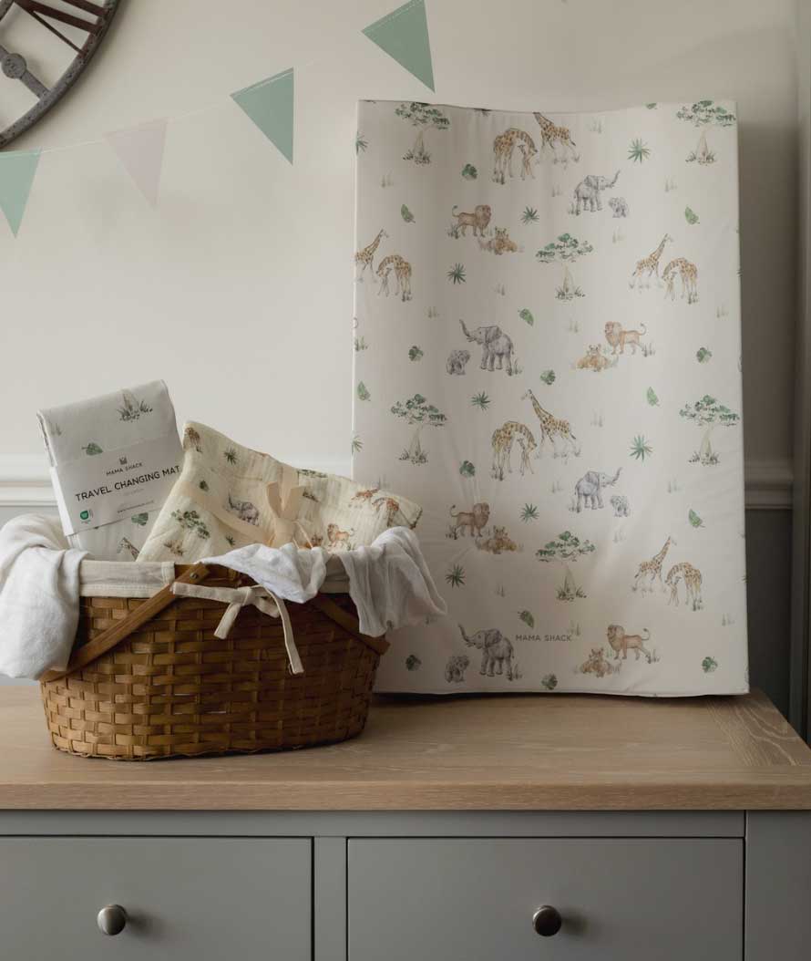 Baby changing table with a basket of items and a sheet with animal pattern on a wooden surface.